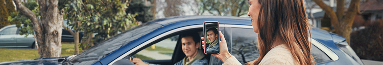 Actor portrayal of a mom taking a picture of her older teenage son driving in a car