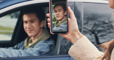Actor portrayal of a mom taking a picture of her older teenage son driving in a car